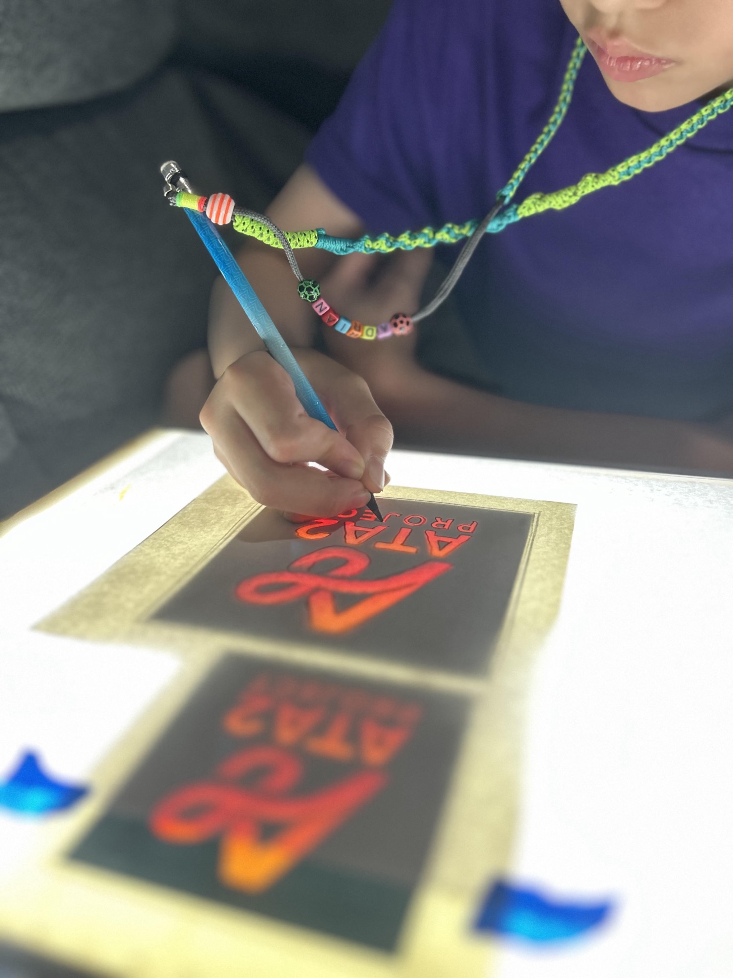 Un niño calca a mano el logo de ATA2 en una mesa de luz, con su strap personalizado al cuello
